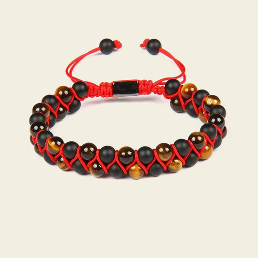 Bracelet with black and brown beads on a red cord against a beige background