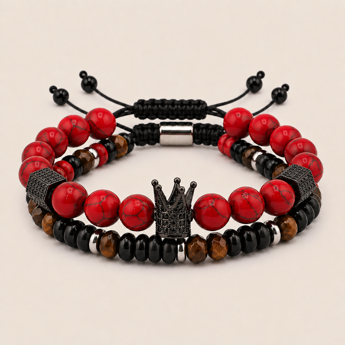 A set of two men's beaded stretch bracelets on a light beige background. The bracelets feature glossy red beads, matte black beads, faceted brown tiger's eye beads, textured black spacer beads, and a central silver-tone crown charm.