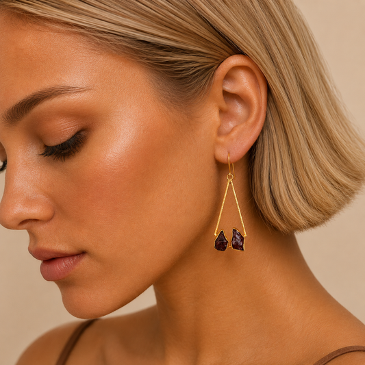 Close-up of a woman wearing gold earrings with purple stones on a beige background