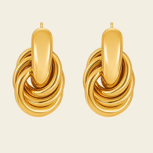 A pair of chunky gold hoop earrings with a twisted, layered rope-like design and smooth polished surfaces, shown on a light beige background.