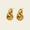 A pair of polished gold huggie hoop earrings with a twisted, knot-like design and post backs, displayed on a clean, solid cream background.