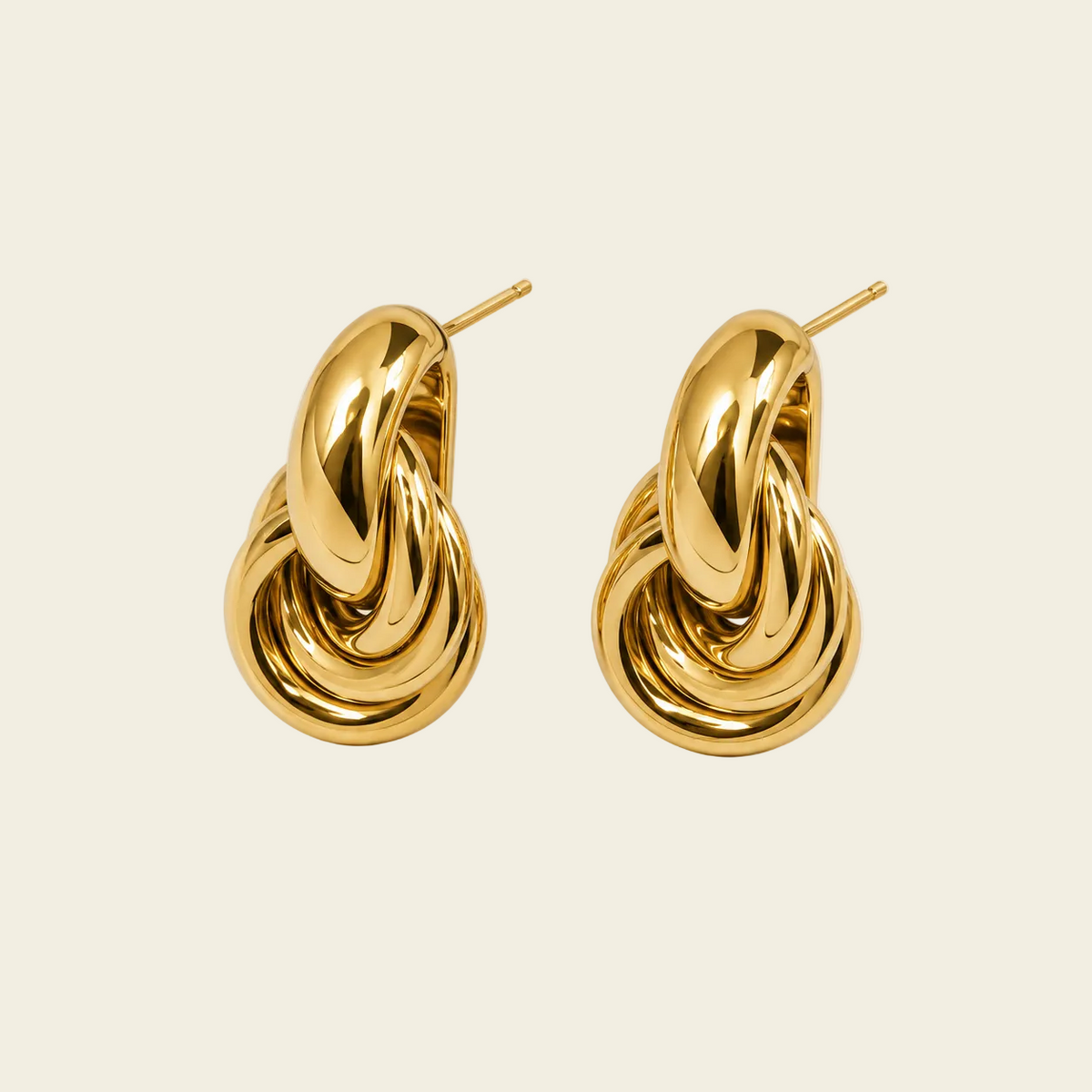 A pair of polished gold huggie hoop earrings with a twisted, knot-like design and post backs, displayed on a clean, solid cream background.