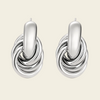 A pair of polished silver-toned hoop earrings with a central elongated oval bar and layered twisted bands below, shown on a plain warm beige background.