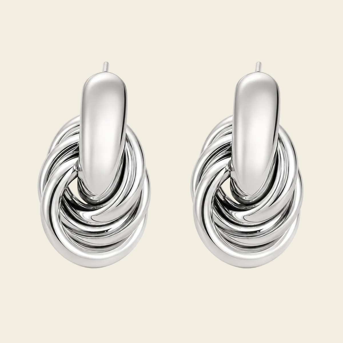 A pair of polished silver-toned hoop earrings with a central elongated oval bar and layered twisted bands below, shown on a plain warm beige background.