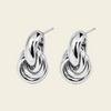 A pair of polished silver-toned earrings with a sculptural, intertwined knot-like design and post backs, displayed on a solid light beige background.
