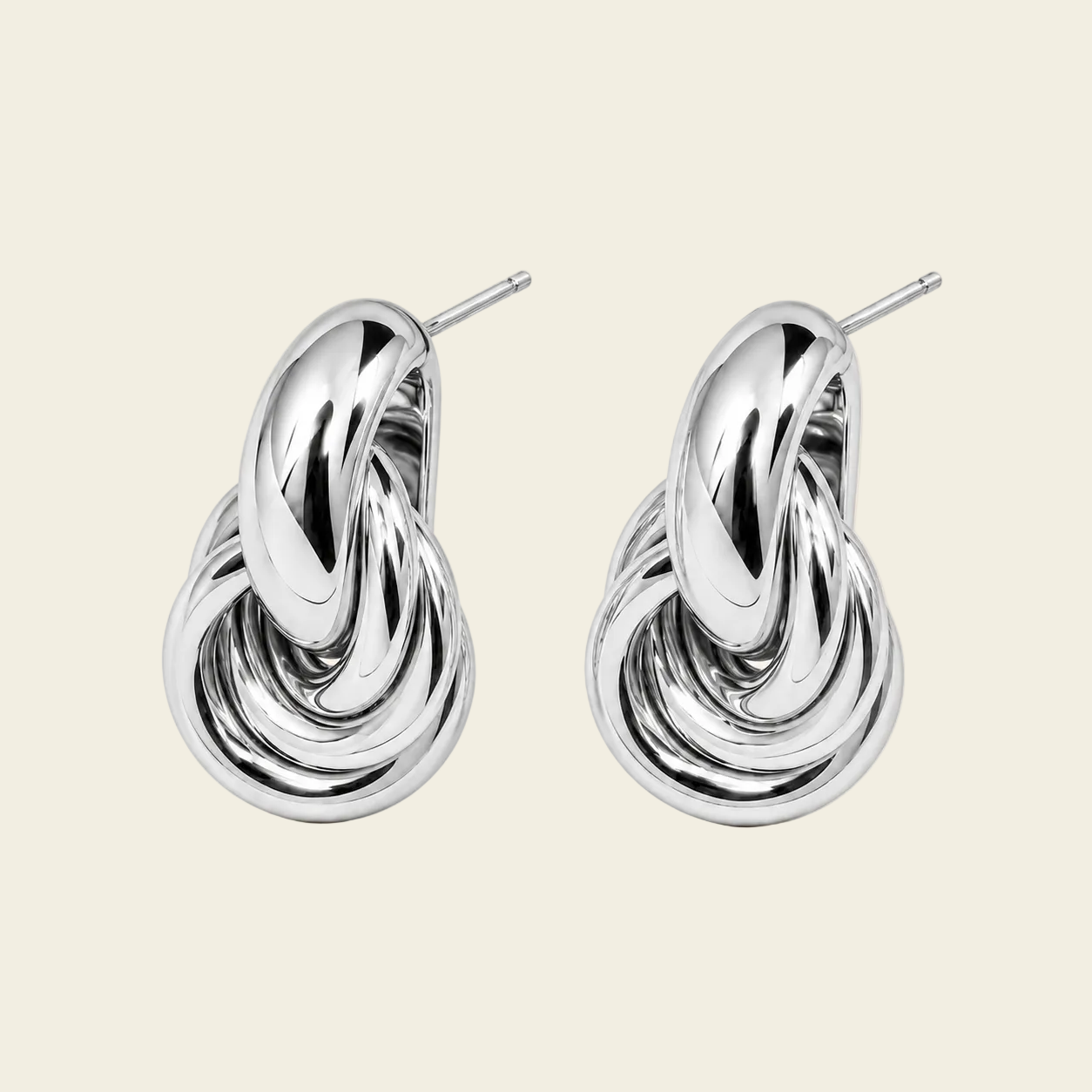 A pair of polished silver-toned earrings with a sculptural, intertwined knot-like design and post backs, displayed on a solid light beige background.