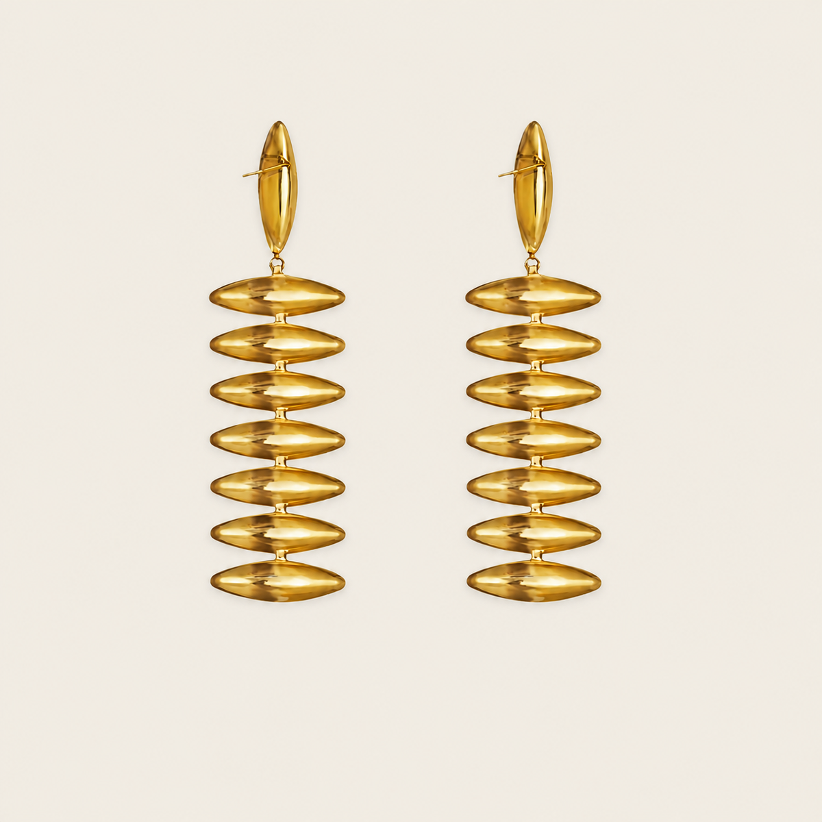 A pair of gold drop earrings with a stacked, ribbed disc design, shown against a solid light beige background.