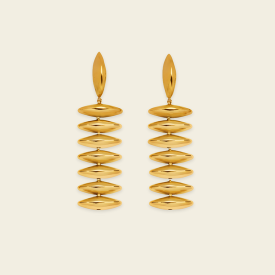 A pair of gold drop earrings with a series of horizontally oriented, polished oval discs hanging from a single elongated teardrop-shaped stud, set against a solid light cream background.