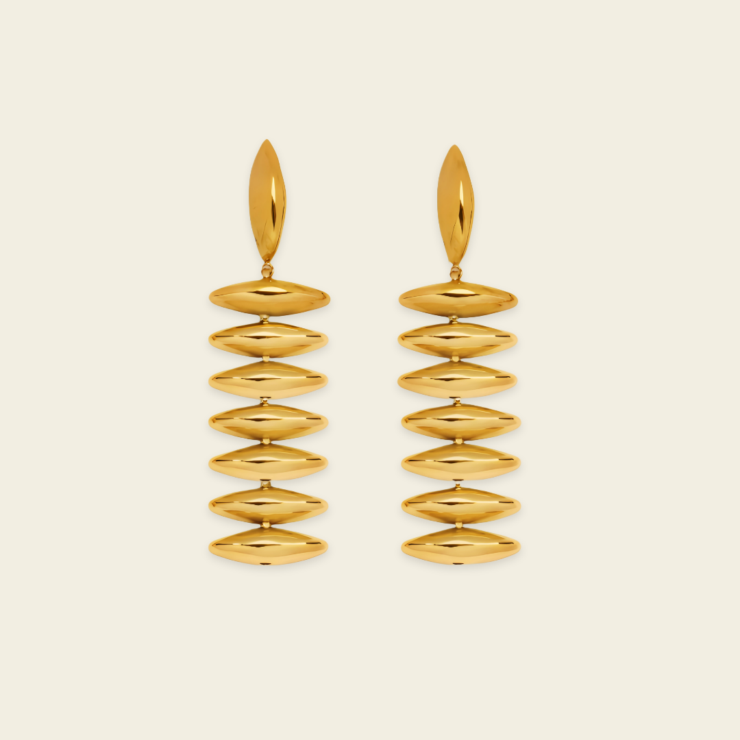 A pair of gold drop earrings with a series of horizontally oriented, polished oval discs hanging from a single elongated teardrop-shaped stud, set against a solid light cream background.