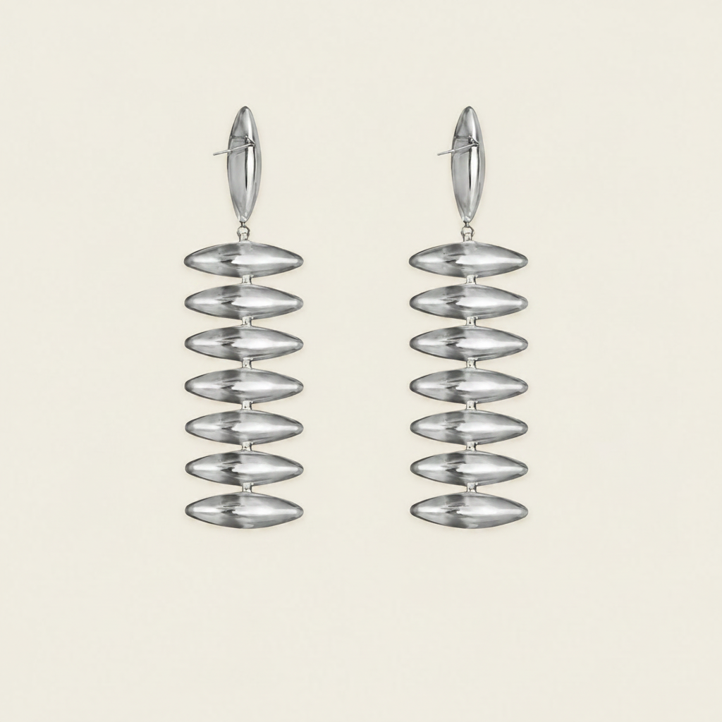 A pair of Silver drop earrings with a stacked, ribbed disc design, shown against a solid light beige background.