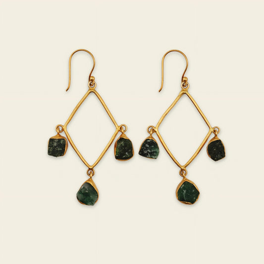 Gold earrings with green gemstones on a beige background