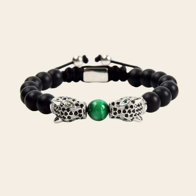 A beaded bracelet featuring matte black round beads, a central polished green oval stone, and two silver-toned panther head charms embellished with small black stones, shown on a light beige background.