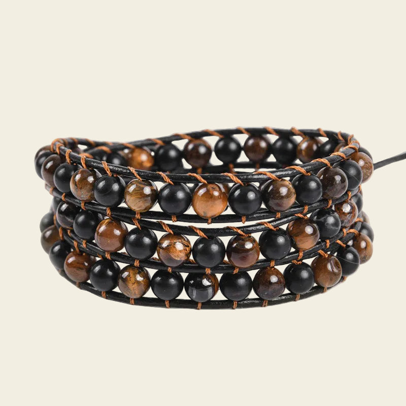 A multi-strand wrap bracelet featuring alternating glossy black and brown tiger's eye beads on a black cord, set against a solid light beige background.