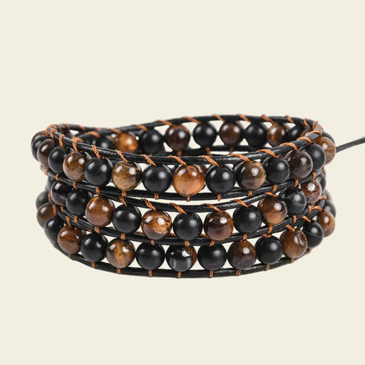 A multi-strand wrap bracelet featuring alternating glossy black and brown tiger's eye beads on a black cord, set against a solid light beige background.