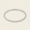 A thin, polished silver bangle bracelet shown on a clean, solid, light cream background.