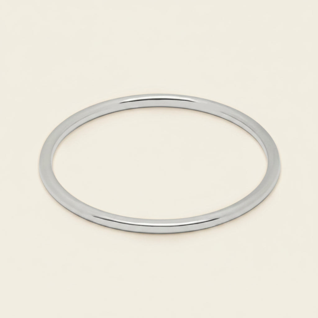 A thin, polished silver bangle bracelet shown on a clean, solid, light cream background.
