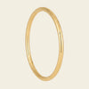 A polished yellow gold bangle ring with a smooth, rounded profile, shown against a solid light beige background.