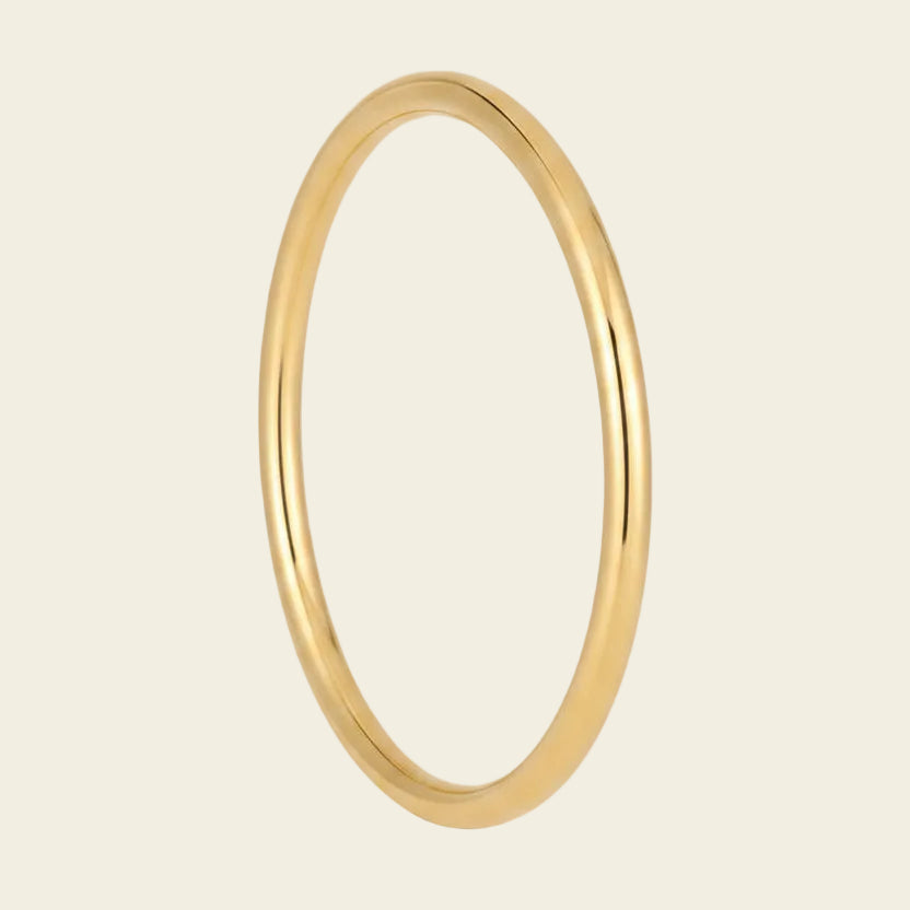 A polished yellow gold bangle ring with a smooth, rounded profile, shown against a solid light beige background.
