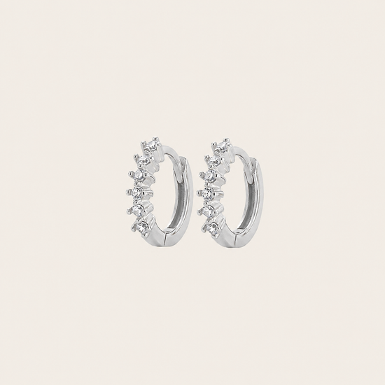 Silver hoop earrings with small diamonds on a light beige background