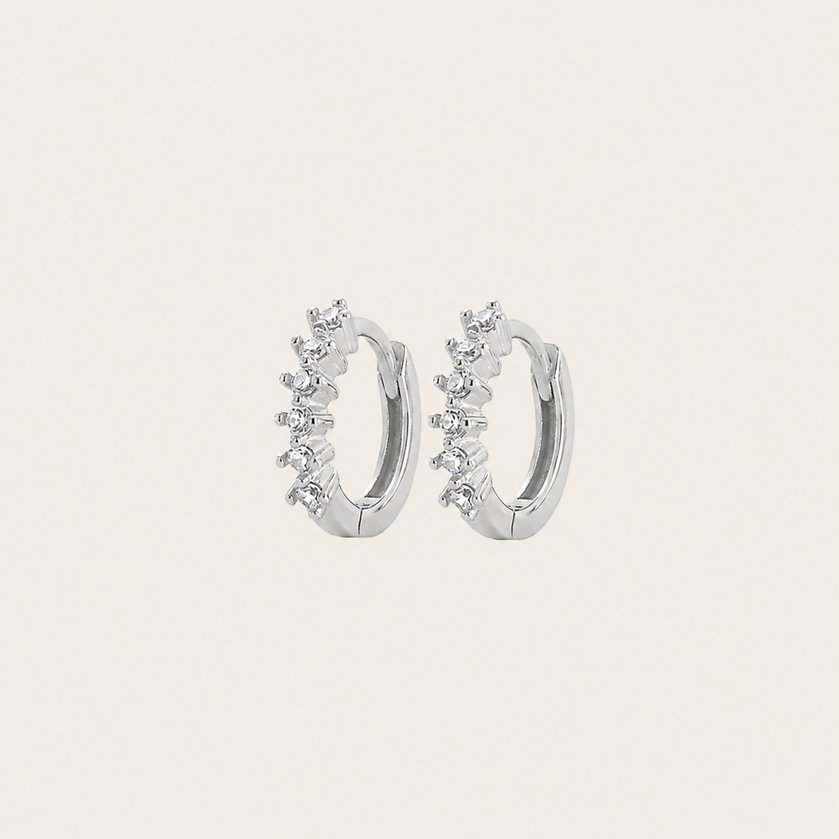 Silver hoop earrings with small diamonds on a light beige background