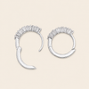 A pair of silver crescent-shaped hoop earrings with a row of clear baguette stones across the top, displayed on a light beige background.