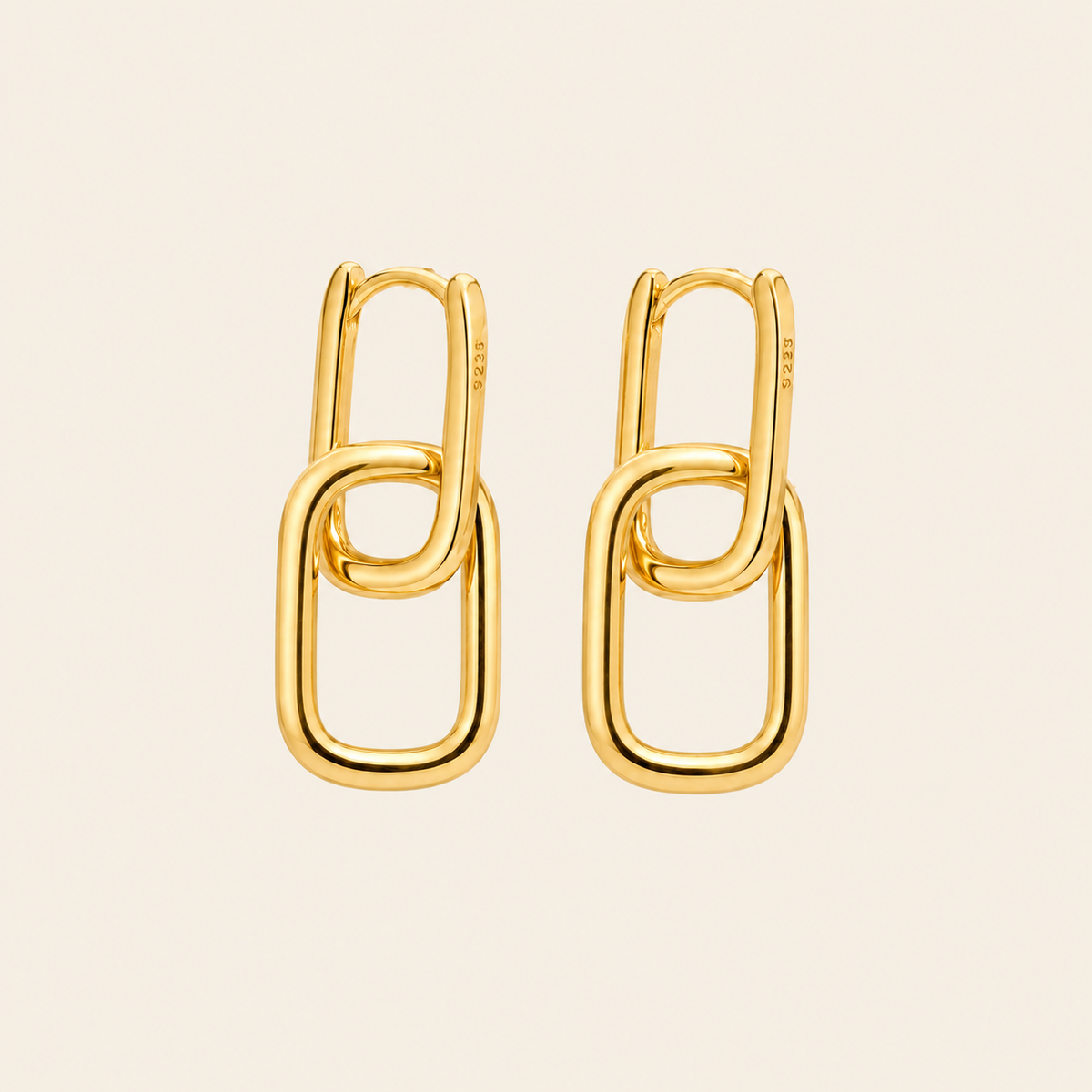 A pair of gold chain-link hoop earrings on a light beige background.