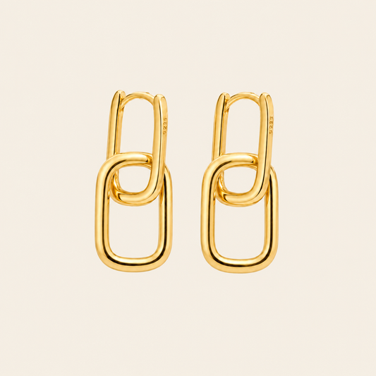 A pair of gold chain-link hoop earrings on a light beige background.