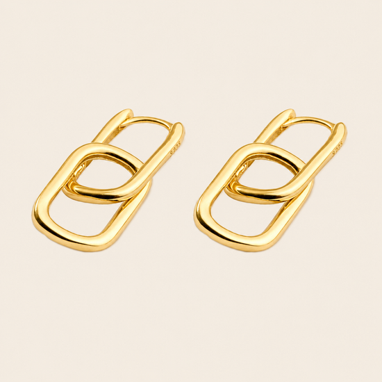 A pair of gold-toned interlocking oval link earrings on a light beige background.