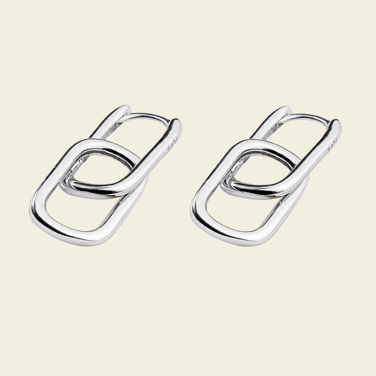 A pair of polished silver-toned interlocking oval link earrings on a solid light beige background.