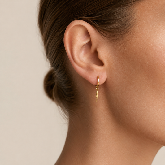 Close-up of an ear wearing a gold earring with a plain background