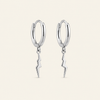 A pair of polished silver hoop earrings with dangling lightning bolt charms, shown against a solid light beige background.