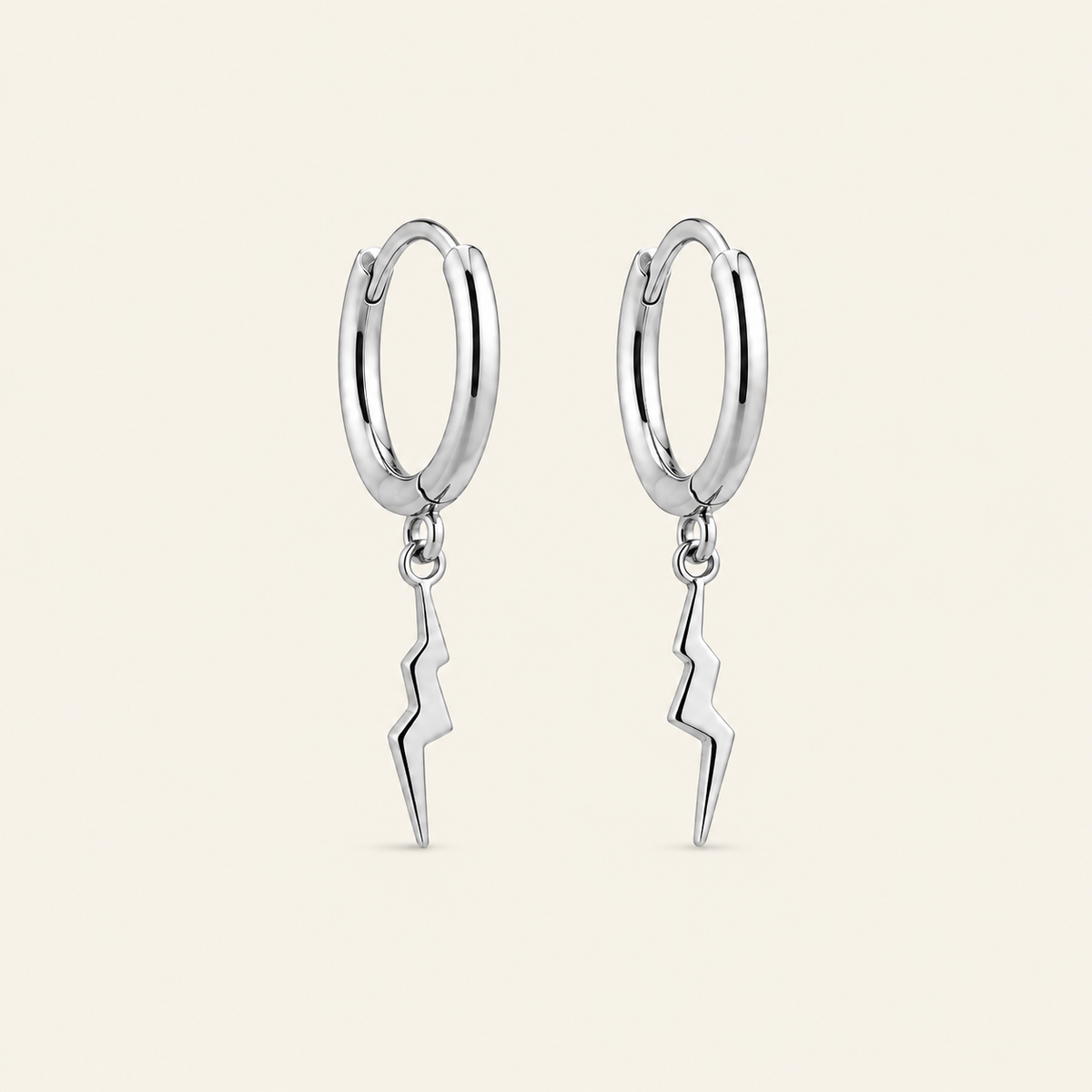 A pair of polished silver hoop earrings with dangling lightning bolt charms, shown against a solid light beige background.