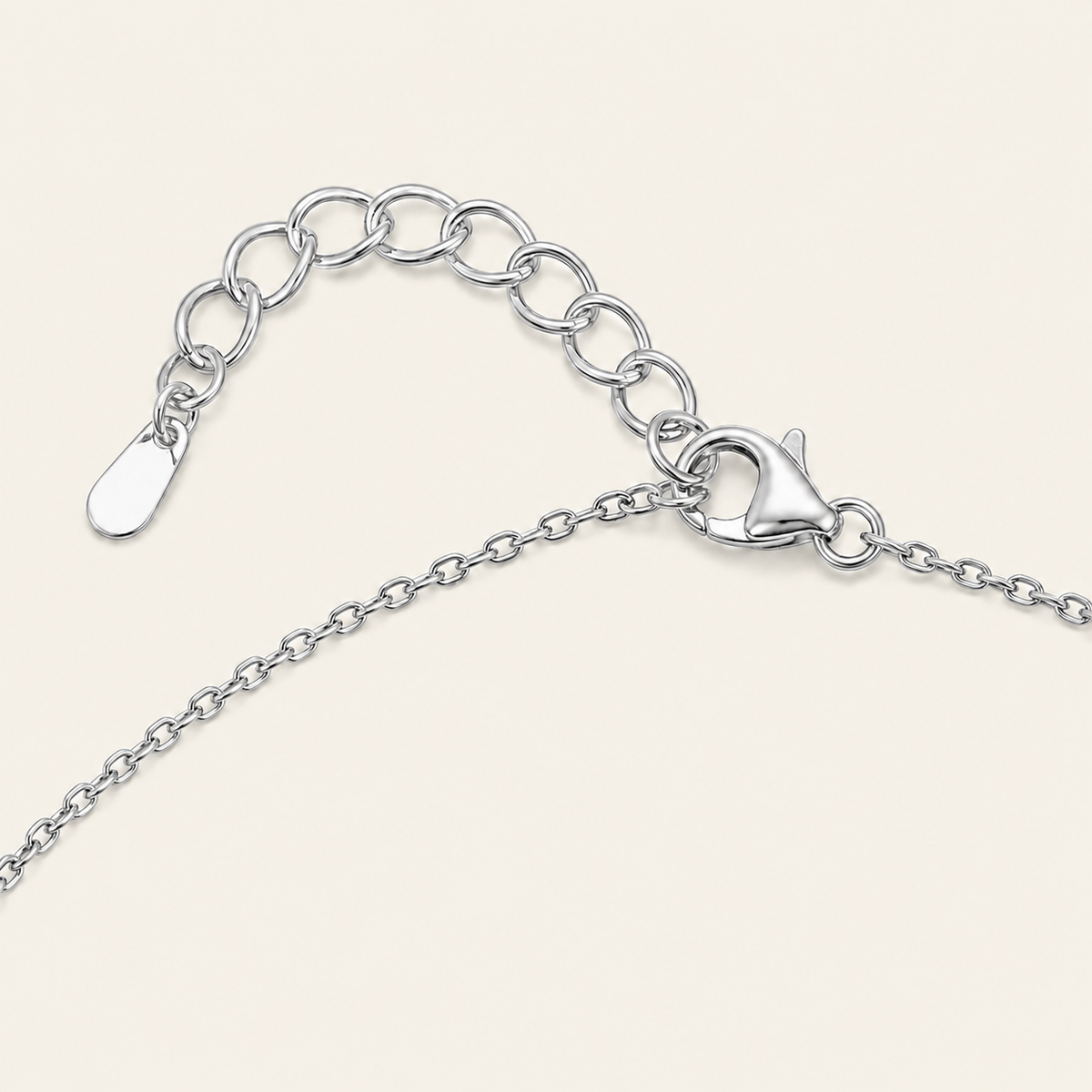 Silver chain necklace with an adjustable lobster clasp and a flat tag, shown on a light cream background.