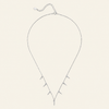 A delicate silver necklace with a V-shaped pendant featuring multiple small spike-like charms, displayed on a solid cream-colored background.
