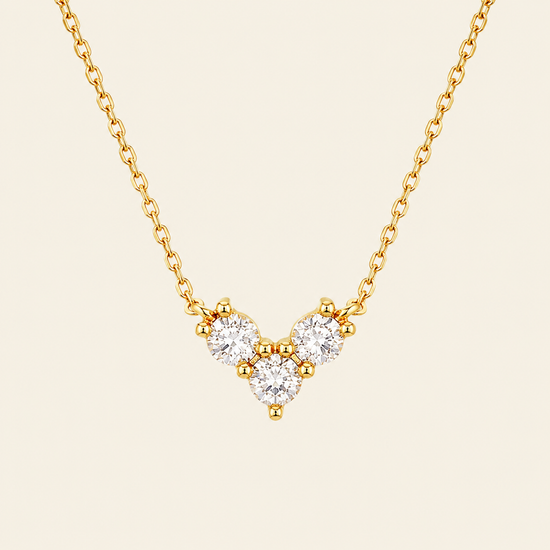 Gold necklace with a V-shaped diamond pendant on a beige background