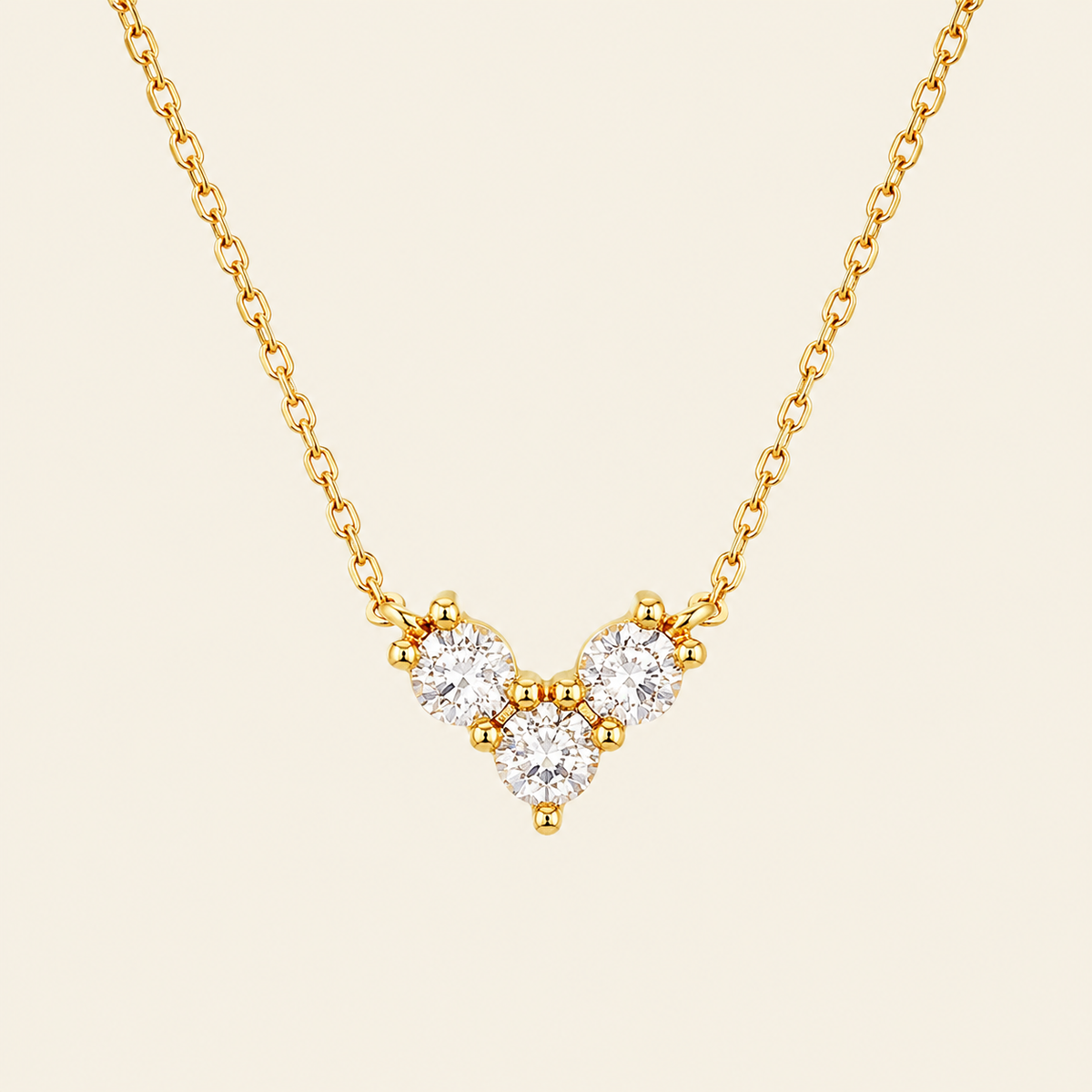 Gold necklace with a V-shaped diamond pendant on a beige background