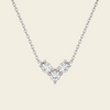 A delicate silver chain necklace featuring a small V-shaped cluster of clear gemstones in a silver setting, displayed against a solid light beige background.