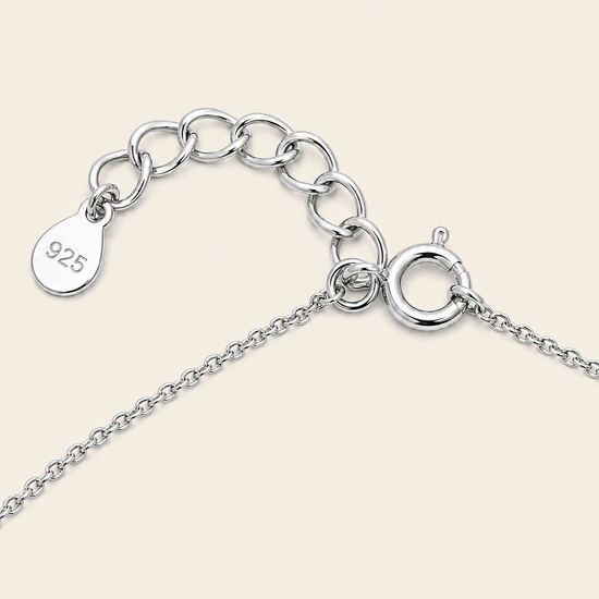 Close-up of a silver chain necklace extender with a lobster clasp and a teardrop-shaped tag engraved with '925' on a light beige background.