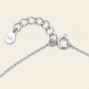 Close-up of a silver chain necklace extender with a lobster clasp and a teardrop-shaped tag engraved with '925' on a light beige background.