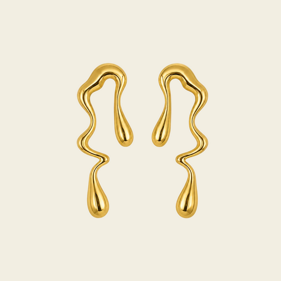 A pair of gold wavy, dripping-shaped earrings on a solid light beige background.