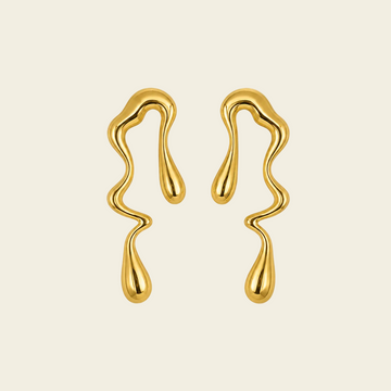 A pair of gold wavy, dripping-shaped earrings on a solid light beige background.