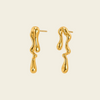 A pair of gold dangling earrings with a dripping, organic wavy shape, shown on a solid pale beige background.
