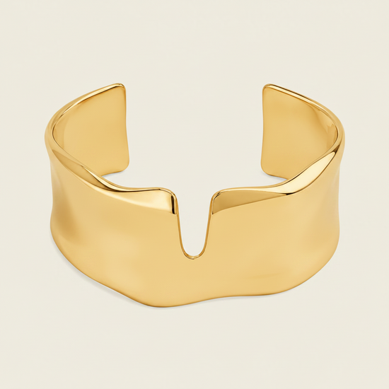A polished silver cuff bracelet with a wide, sculptural, wavy profile and a central V-shaped notch, shown on a solid light beige background.
