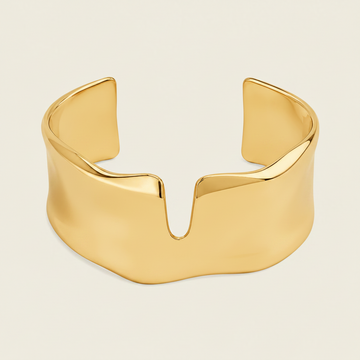 A polished silver cuff bracelet with a wide, sculptural, wavy profile and a central V-shaped notch, shown on a solid light beige background.