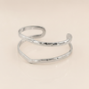 A silver-colored open cuff bangle with a hammered texture, displayed on a clean, light beige background.