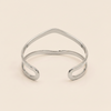 A polished gold open cuff bangle with a wavy, organic line design, photographed on a solid light beige background.