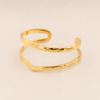 A gold-colored open cuff bangle with a hammered texture, displayed on a clean, light beige background.