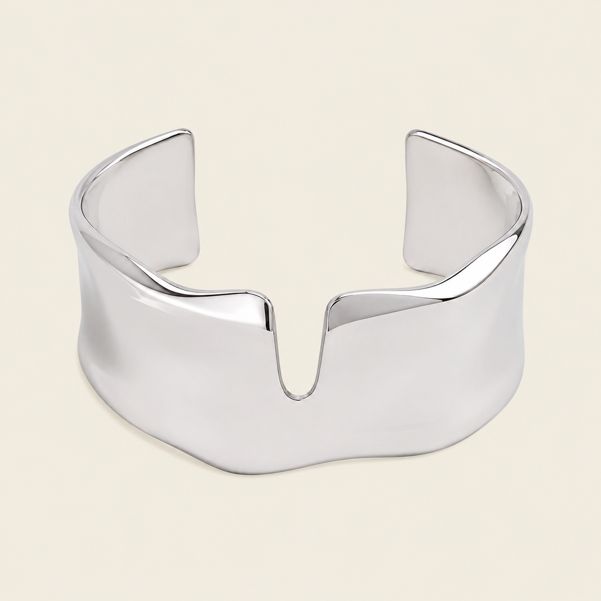 A polished silver cuff bracelet with a wide, sculptural, wavy profile and a central V-shaped notch, shown on a solid light beige background.
