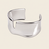 A polished silver cuff bracelet with a unique wavy, open design, shown on a solid light beige background.
