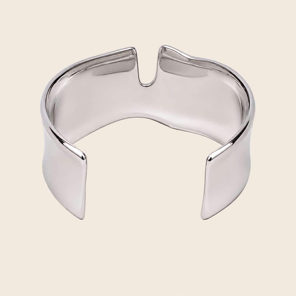 A polished silver-toned metal cuff bracelet with a unique curved, open design, shown on a solid light beige background.